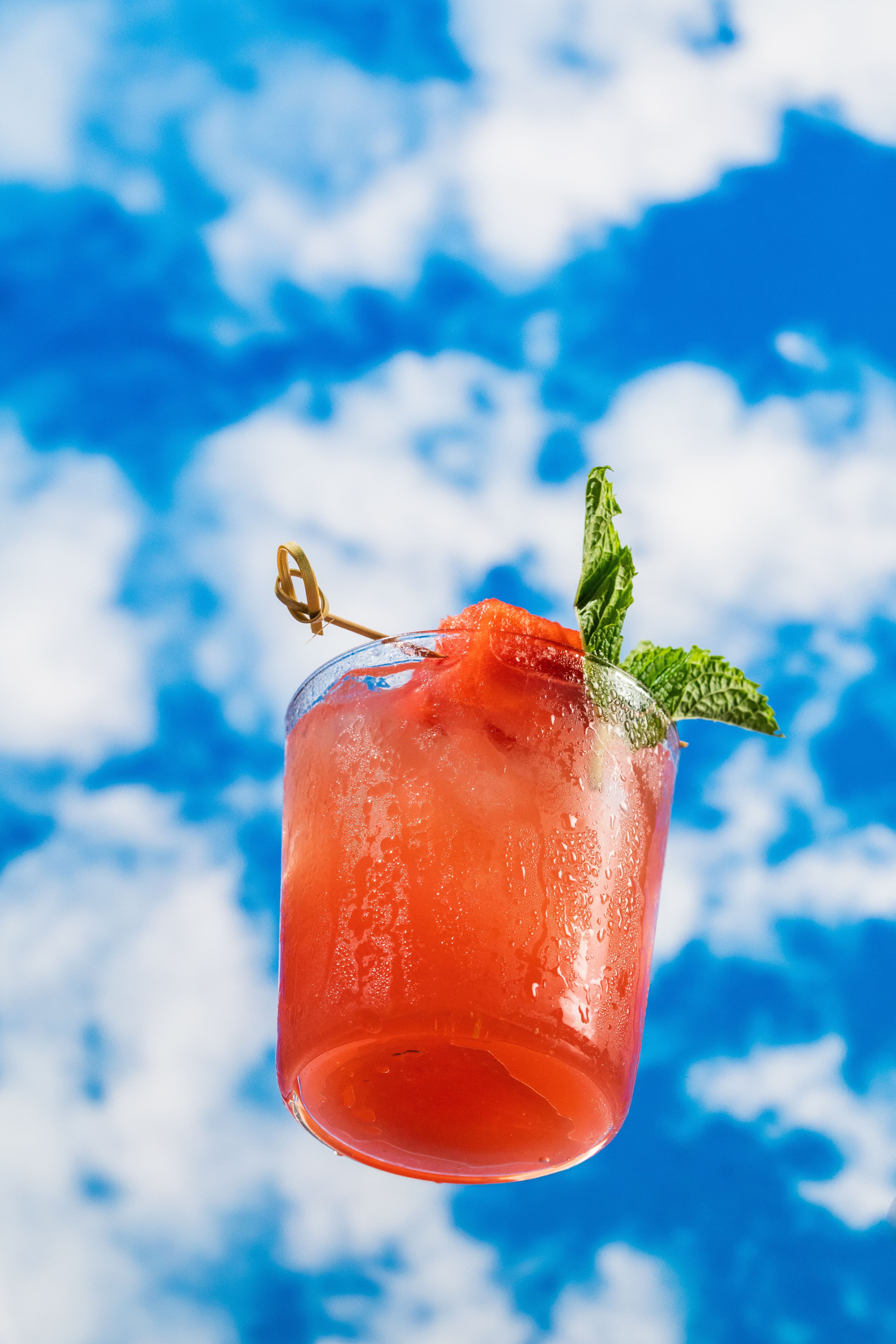 A red summer cocktail with mint photographed against a bright blue sky.