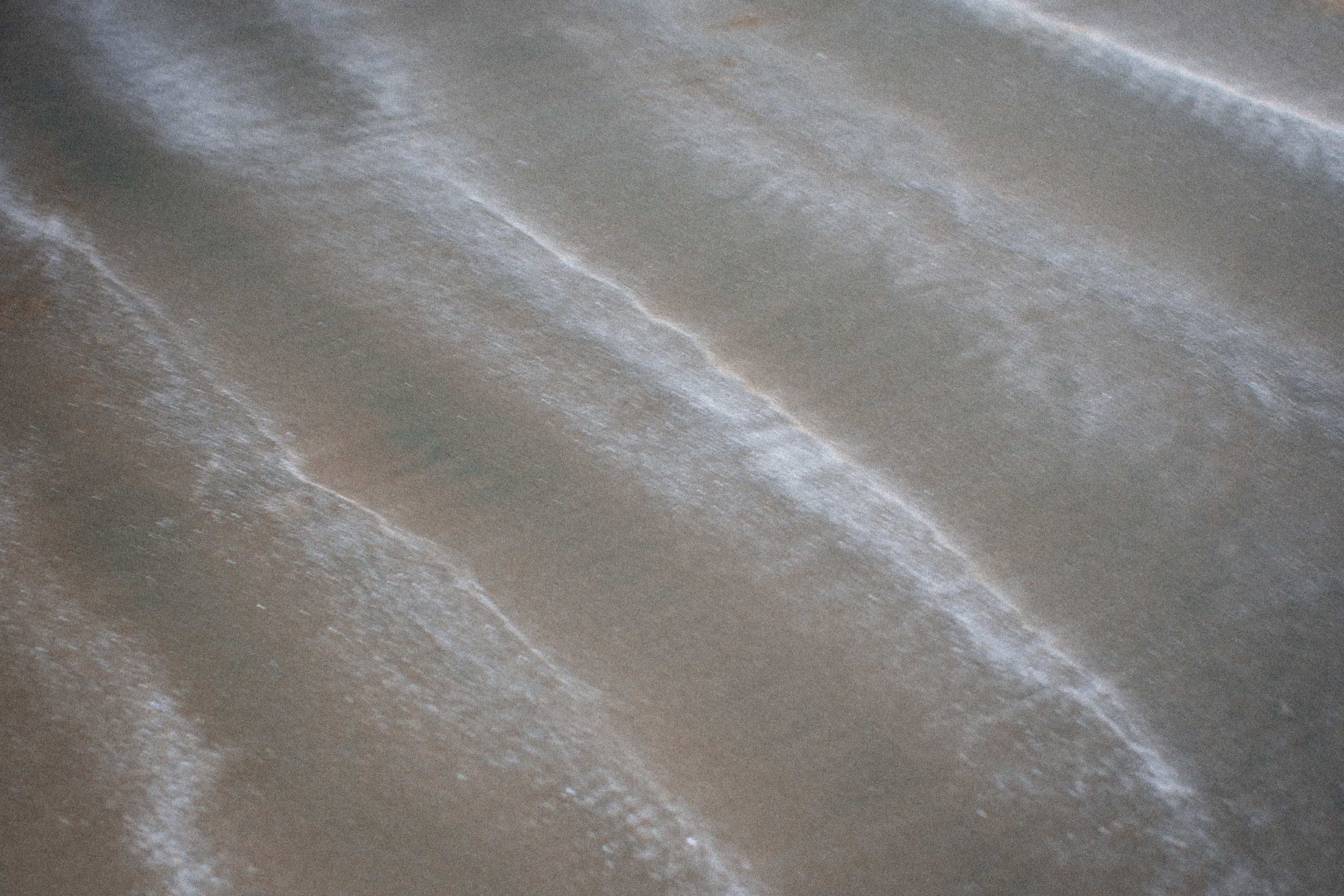 Soft bands of light moving across a calm grey water surface.