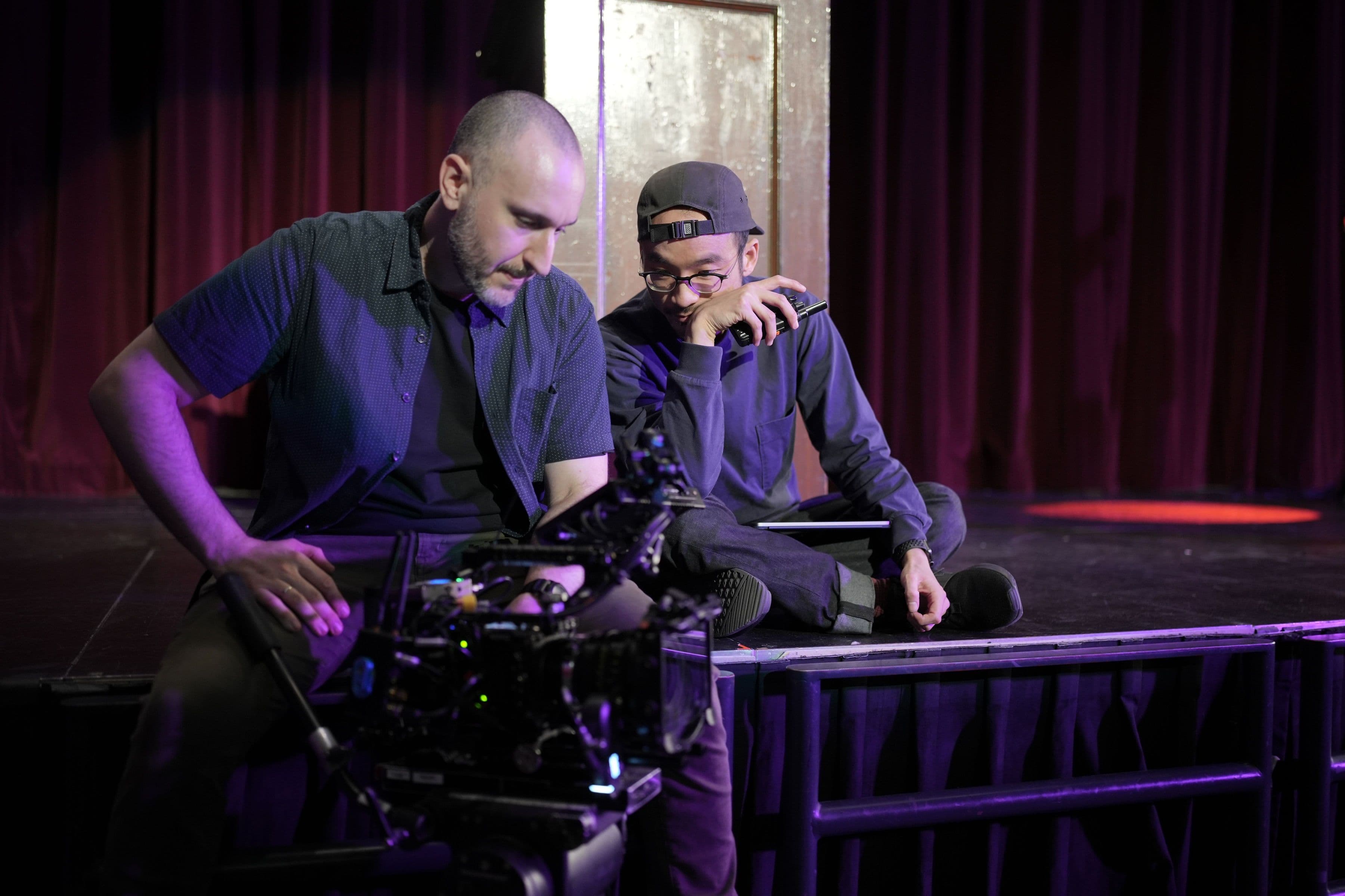 Two crew members checking a cinema camera beside the theatre stage.