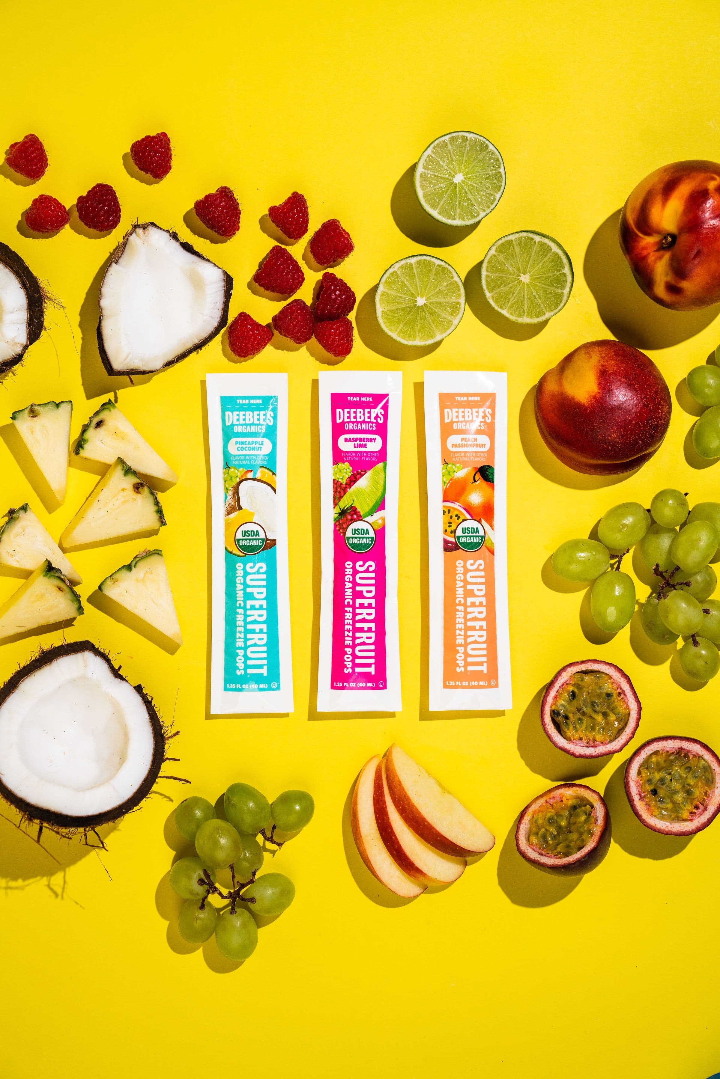 DeeBee’s SuperFruit freezies arranged with fresh fruit on a bright yellow background.