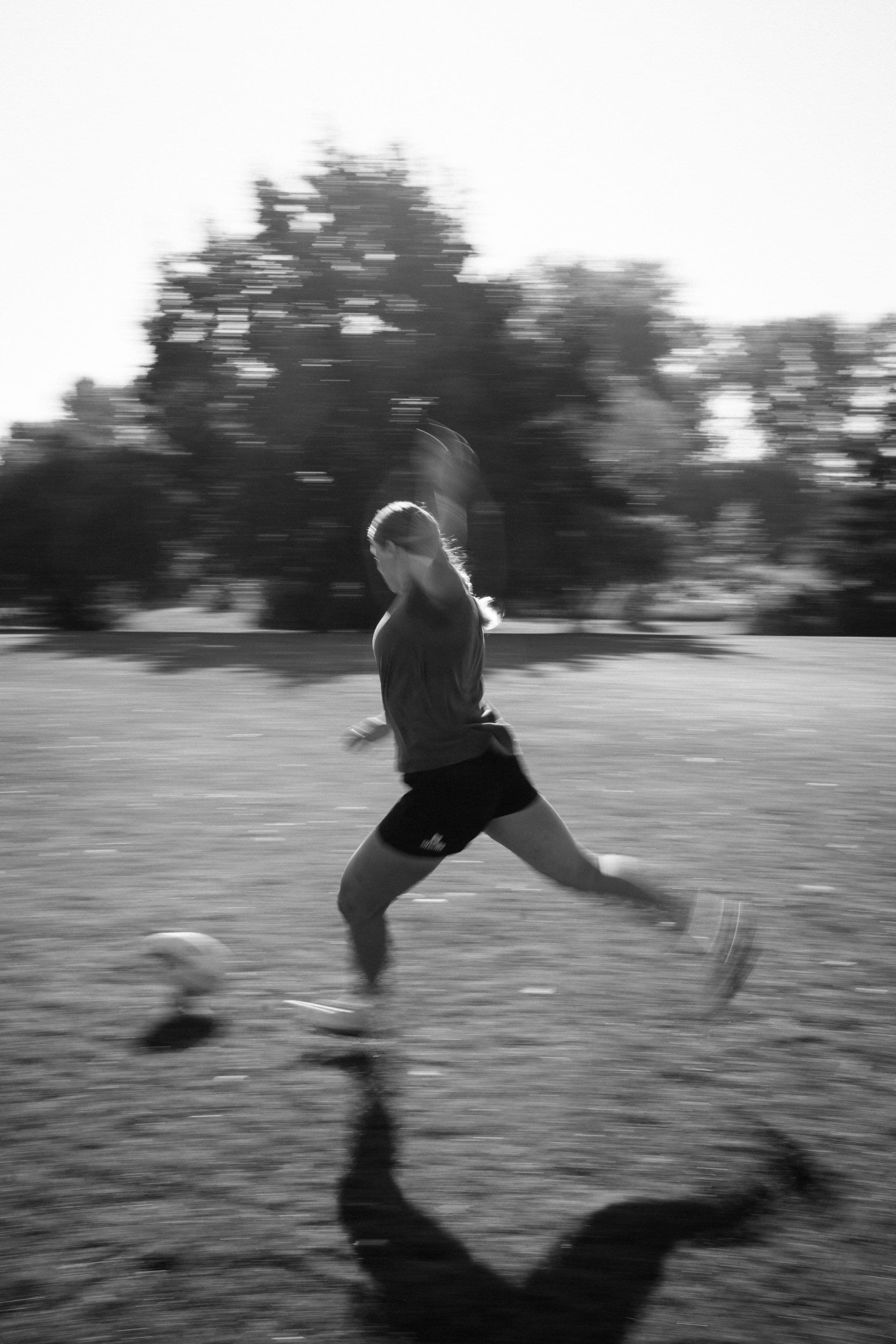 Black-and-white photograph of Sophie de Goede kicking a rugby ball on a grass field.