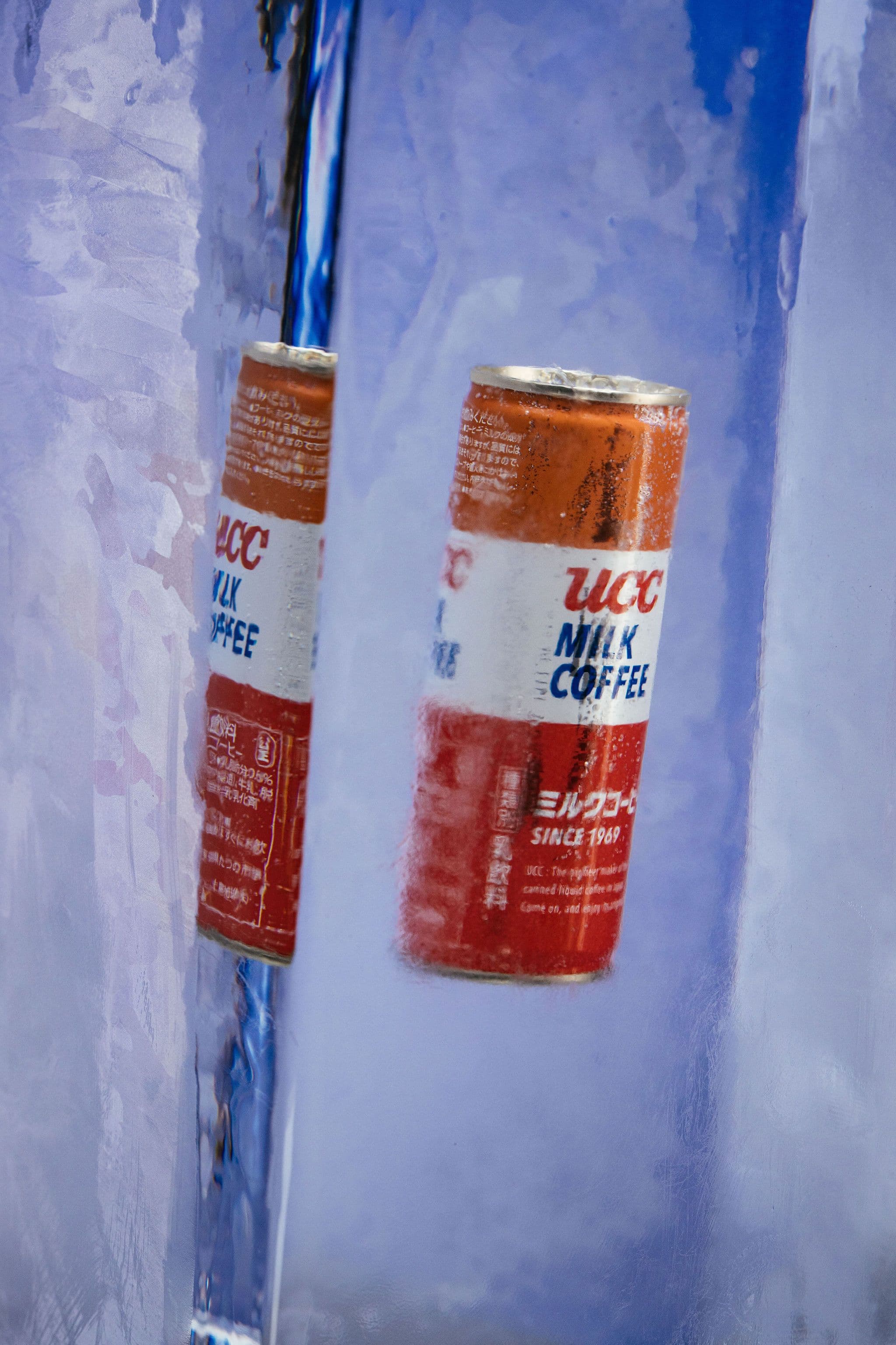 Two cans of UCC Milk Coffee frozen inside a tall translucent ice block.