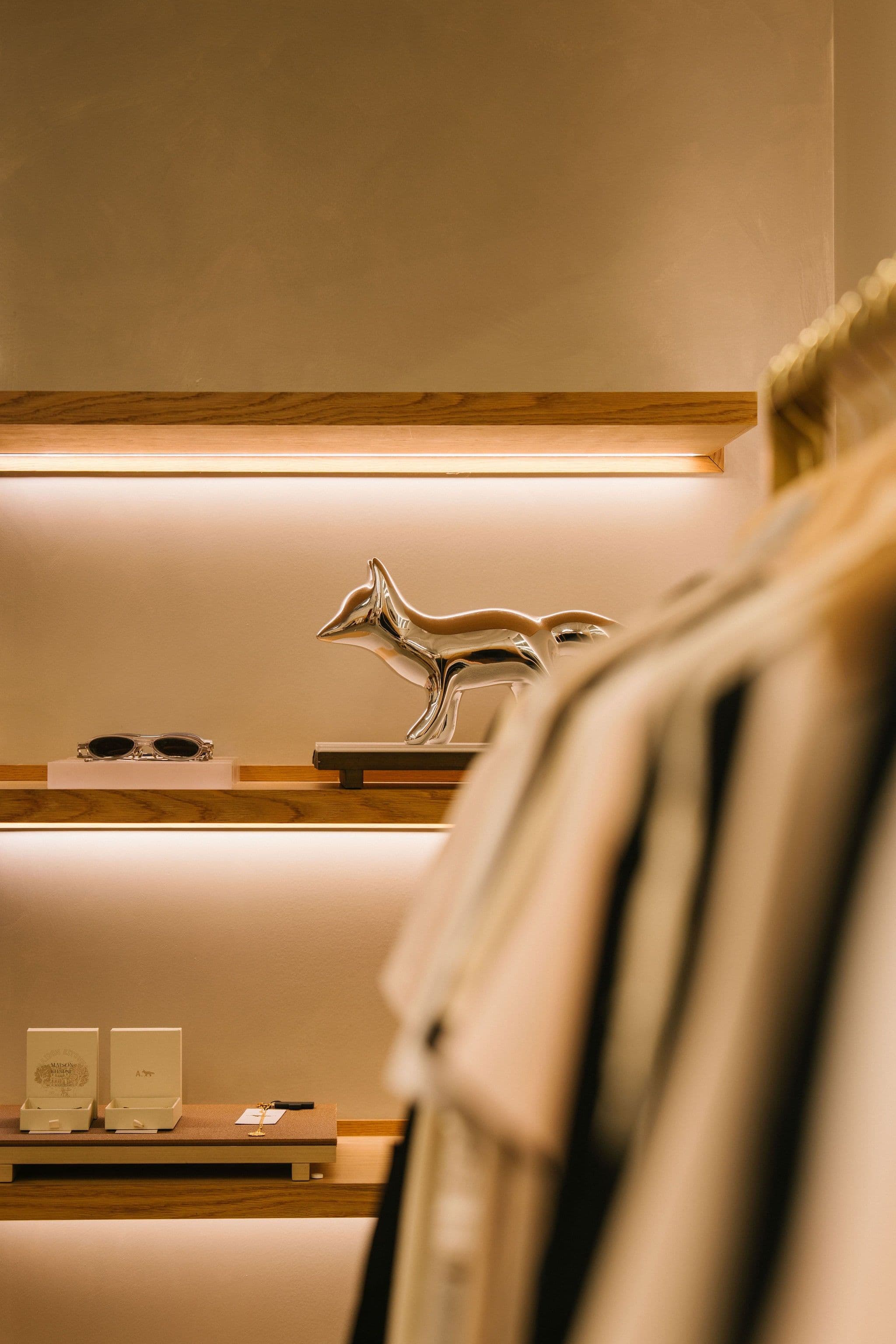 Fox sculpture on a warmly lit display shelf beside a clothing rail in the Kitsuné boutique.
