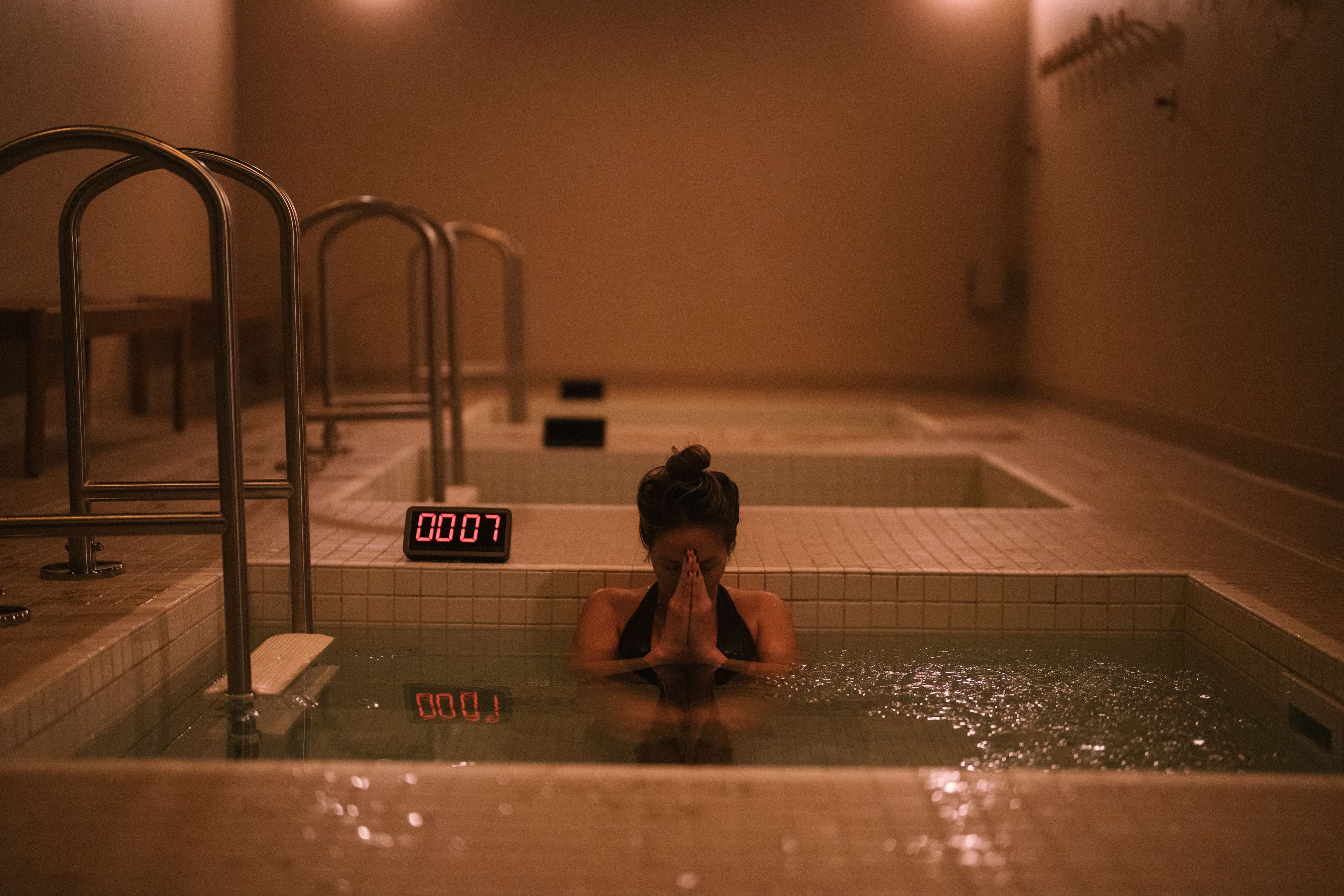 A guest immersed in a Tevah cold plunge beside a small digital timer.