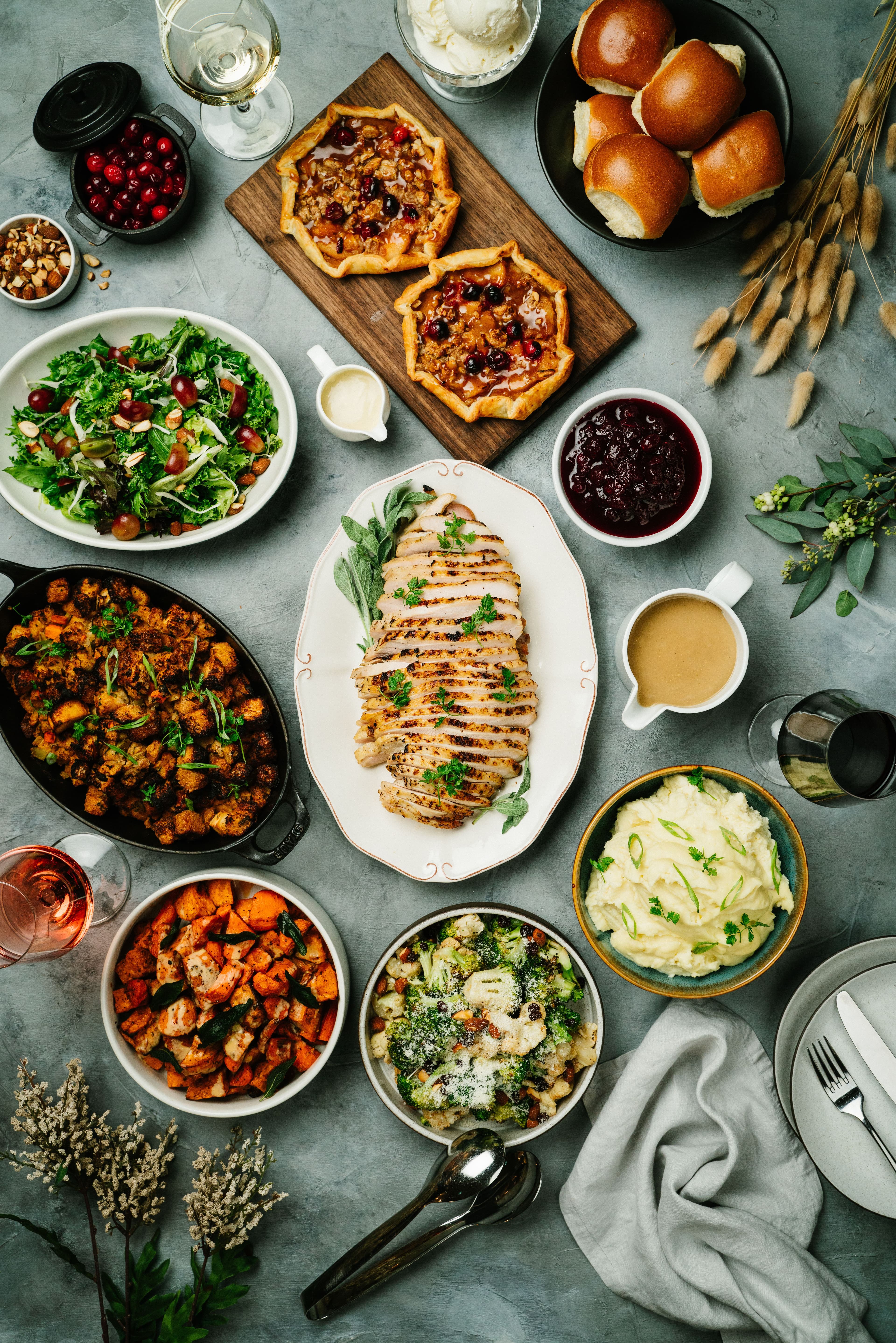 An overhead holiday dinner spread with turkey, vegetables, bread, and side dishes.