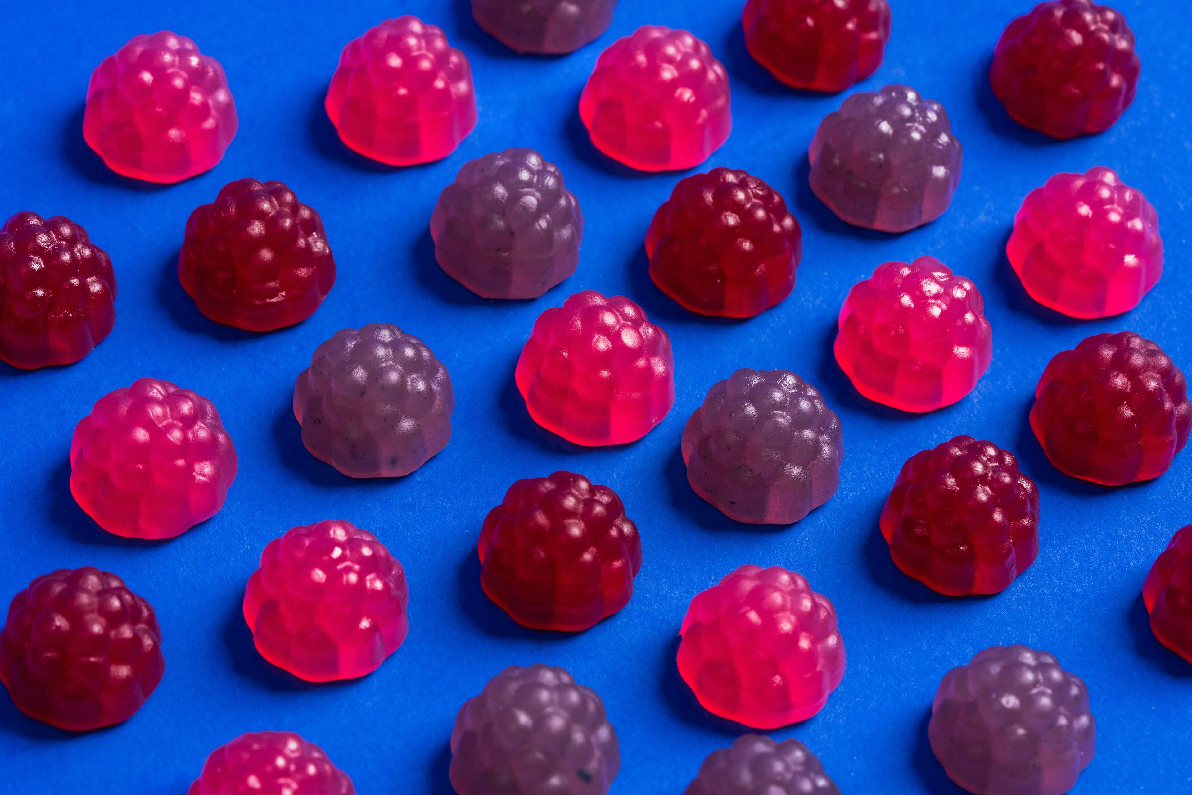 Red, pink, and purple SmartSweets berry gummies arranged across a blue surface.