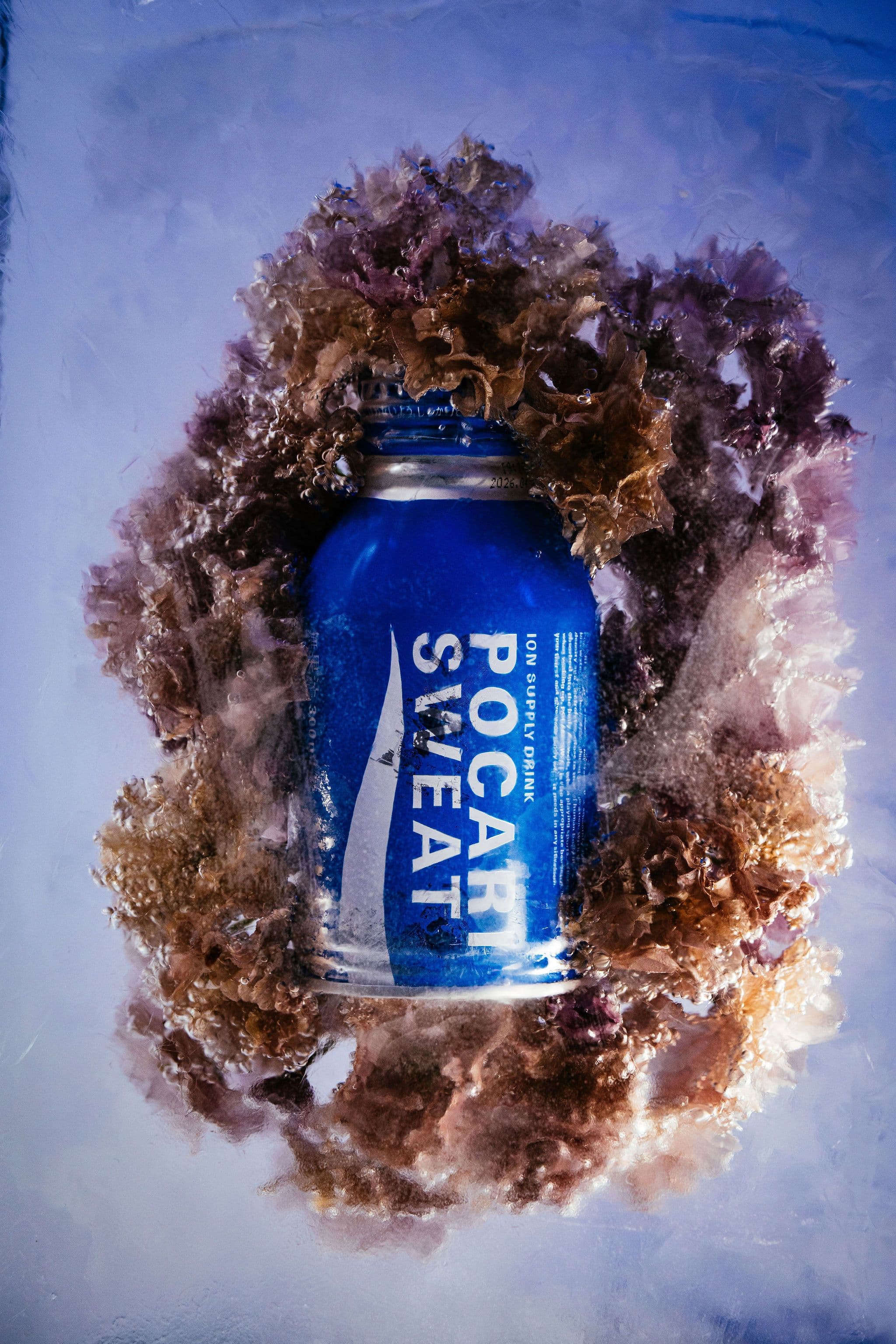 A blue Pocari Sweat can encased in ice and framed by frozen ruffled flowers.