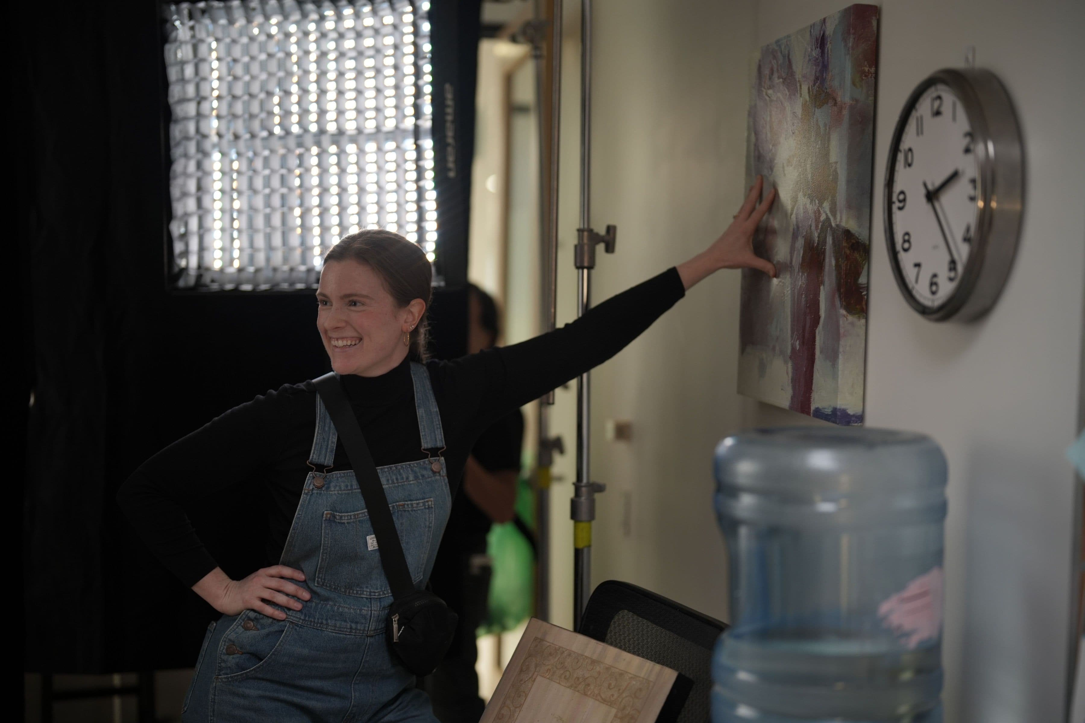 A crew member checking a wall poster beside a water cooler, with a film light behind her.