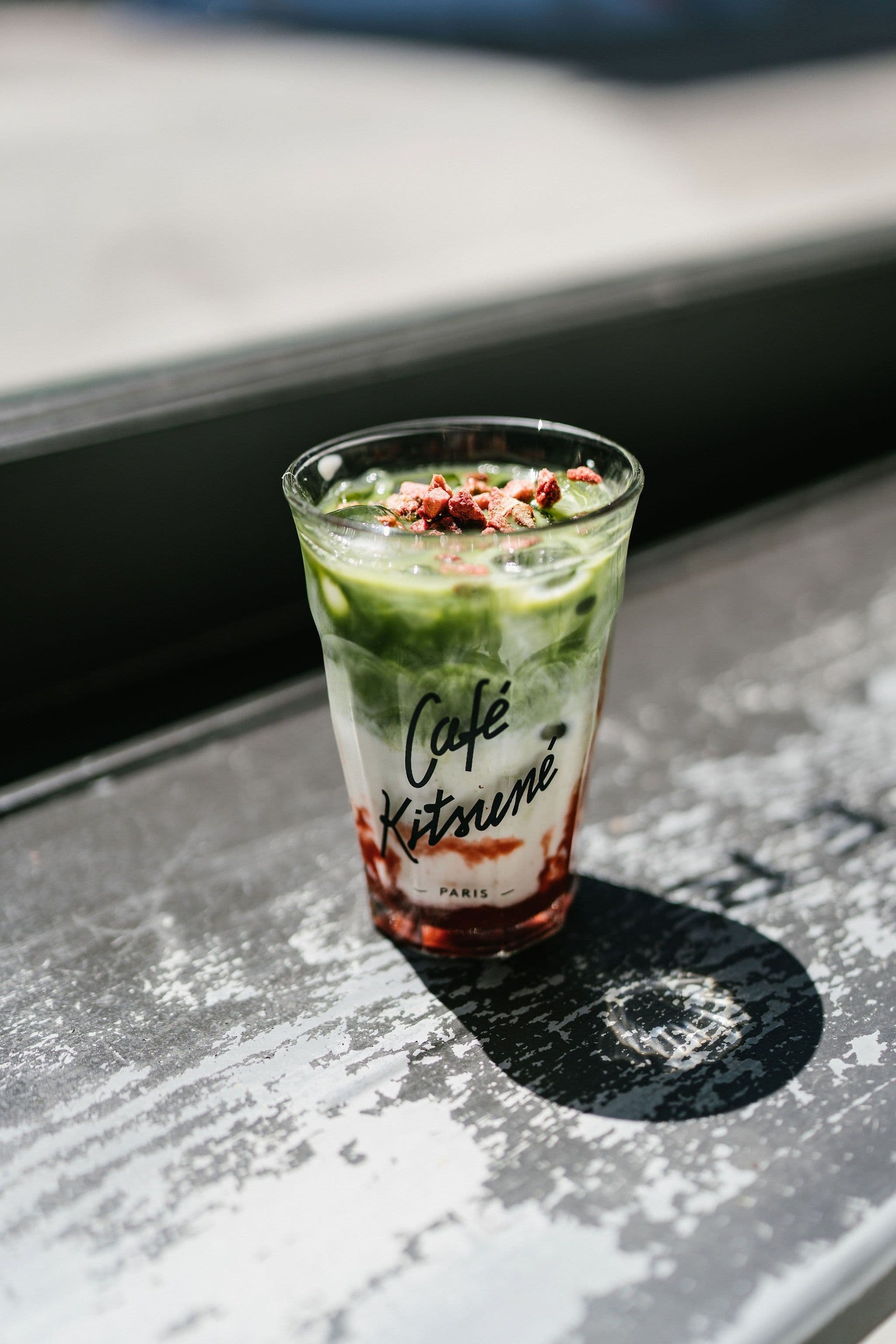 Layered green iced drink in a Café Kitsuné glass on a sunlit stone counter.
