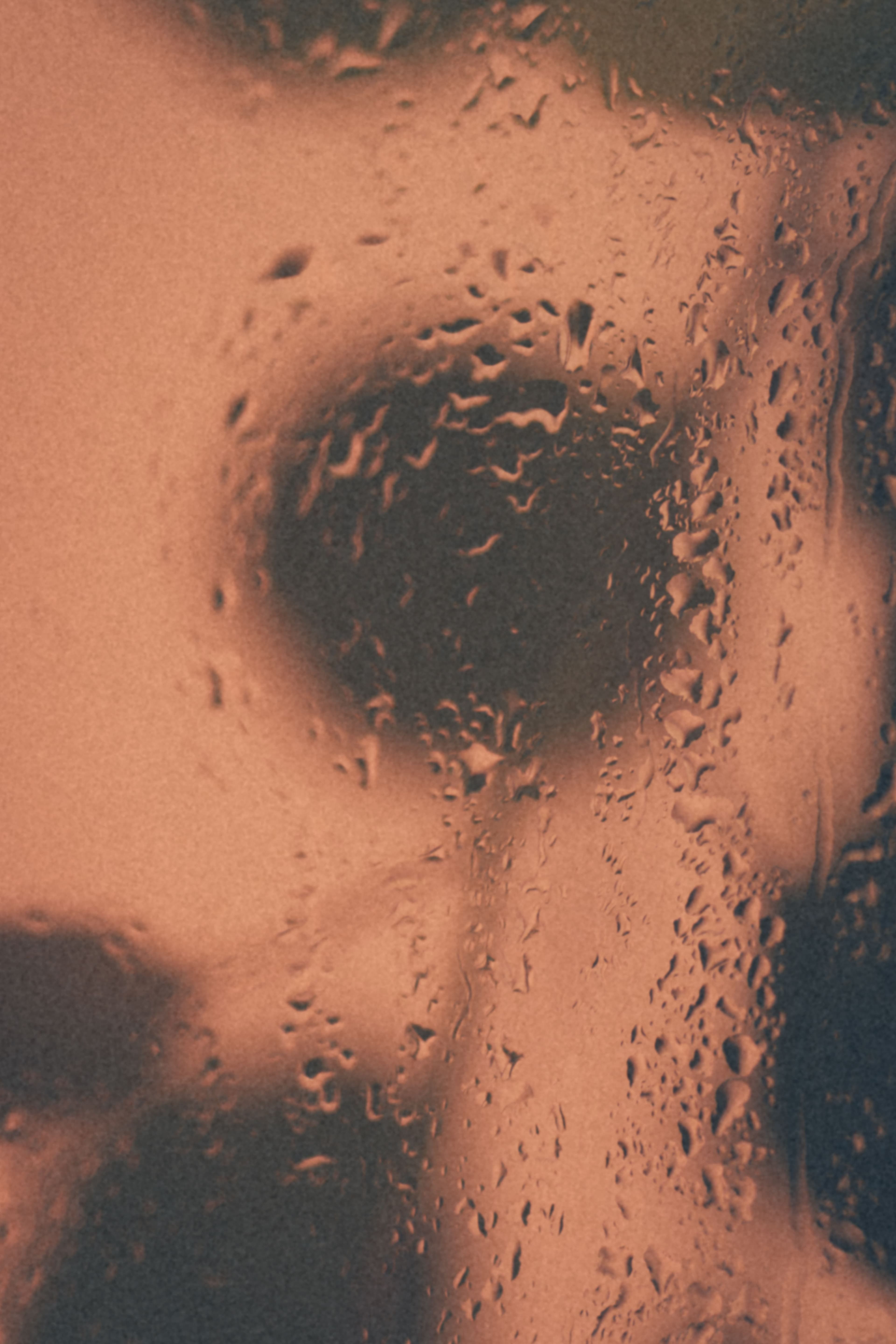 A softly obscured figure seen through a condensation-covered glass wall.