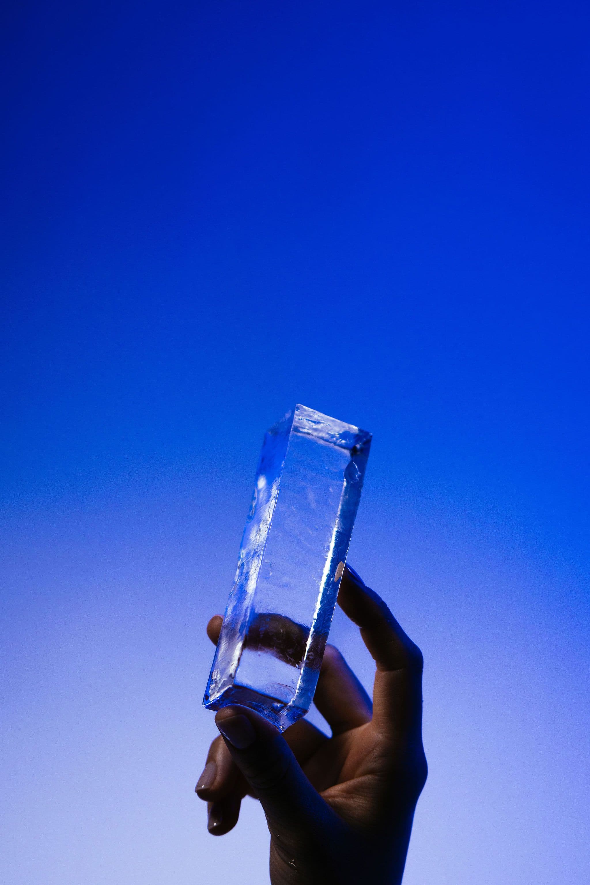A hand angles a tall clear ice column towards the light against a blue background.